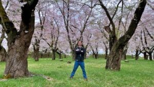 Man stands confidently among blooming cherry trees in Tsuruga Castle gardens, embodying the potential of Aizu's natural and cultural assets for tourism.