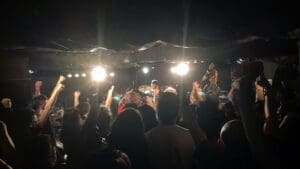 The view from the crowd at a Japan heavy metal concert, showing fans with fists in the air in front of a brightly lit stage in a small, underground venue.