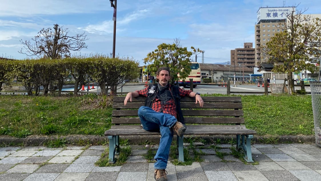 Man sits on a bench outside Aizuwakamatsu Station thinking about the Aizu strategy illustrating the urban environment and logistical access point for rural Japan's tourism.