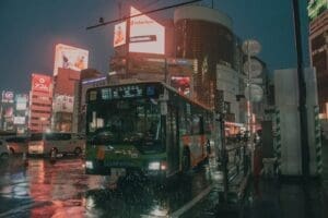 Busy Tokyo street at night with neon signs and a city bus, illustrating the vibrant yet crowded Impact of current Travel Policy and departure tax on urban Japan.